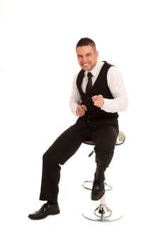 The photo shows a young man,in a business outfit,sitting on a bar stool and grinning exaggeratedly into the camera.