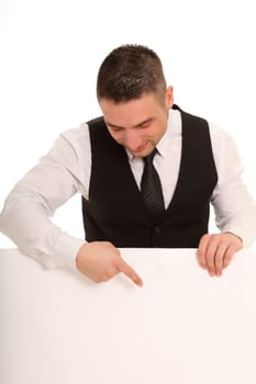 A young man stands behind an advertising sign,looks at it and also points a finger at it.