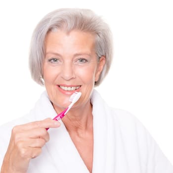 Studio shot of an elderly woman in a white bathrobe and using a toothbrush