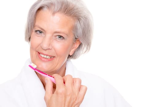 Studio shot of an elderly woman in a white bathrobe and using a toothbrush