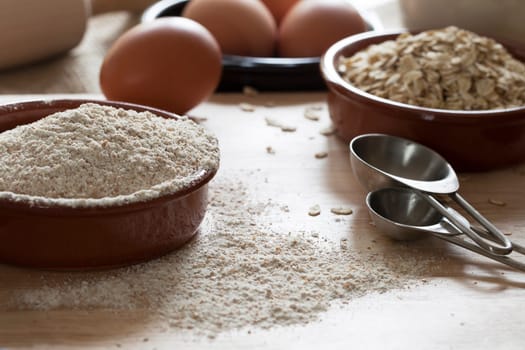 Bowl of whole wheat flour and rolled oats with measuring spoons and eggs in background