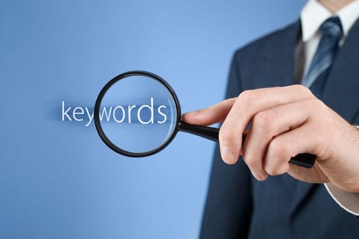Keywords analysis, look for, search for and seek concept. Man with magnifying glass and text keywords.