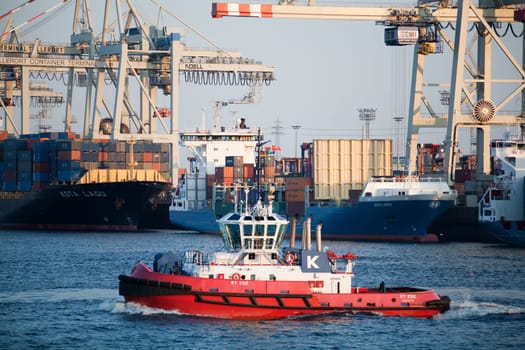 Tugboat crossing the busy Elbe River in Hamburg Harbor, Germany, with freighters in background.