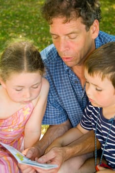 father with daughter and son reading in park