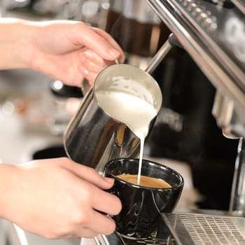 Waitress hands pouring milk making cappuccino