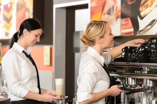 Two waitresses serving coffee with machine in shop