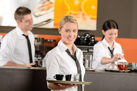 Confident waitress serving coffee with tray colleagues working behind