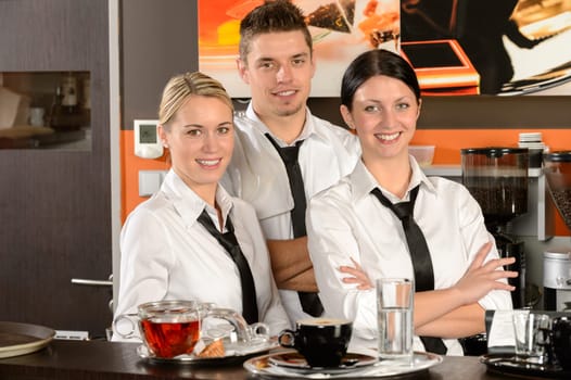 Three smiling server posing in uniform in cafe