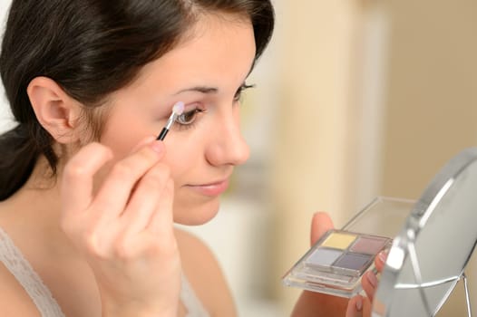 Young girl applying eyeshadow on eyelid looking at mirror