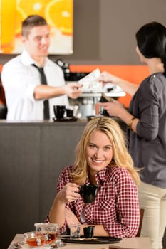 Happy female customer drinking espresso in cafe looking at camera