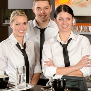 Three smiling server posing in uniform in cafe