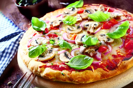 Delicious vegetarian pizza topped with tomato, melted cheese, mushrooms, onions and fresh basil leaves served on a wooden board, high angle view. More pizza at my port.