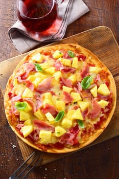 Overhead view of a delicious freshly baked ham and pineapple pizza on a thin crispy crust standing on an old wooden board on a kitchen table. More pizza at my port.