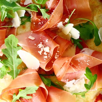 Delicious thinly sliced Italian prosciutto ham and fresh rocket leaves served as a topping on a pizza base, closeup view
