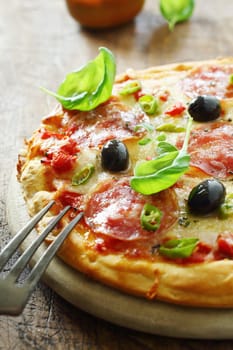 Savoury Italian salami pizza on a crisp golden crust with basil, chilli pepper, olives and cheese on tomato paste served on an old rustic wooden board. More pizza at my port.
