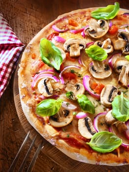 Closeup high angle view of a freshly baked tasty mushroom and onion pizza with a crisp golden crust garnished with fresh basil leaves and served on a wooden board