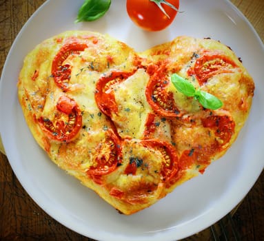 Overhead view of a romantic heart shaped Italian pizza topped with a vegetarian topping of golden melted cheese and tomato on a plain white plate. More pizza at my port.