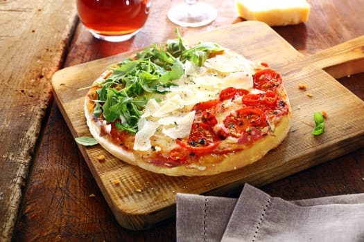 Colourful Italian pizza in the national colours topped with fresh green rocket leaves, white shavings of cheese and red tomatoes in three stripes standing on a wooden board on an old rustic table