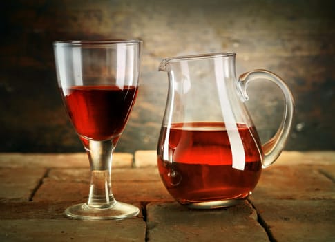 A glass of red wine with a jug of wine on a rustic table.