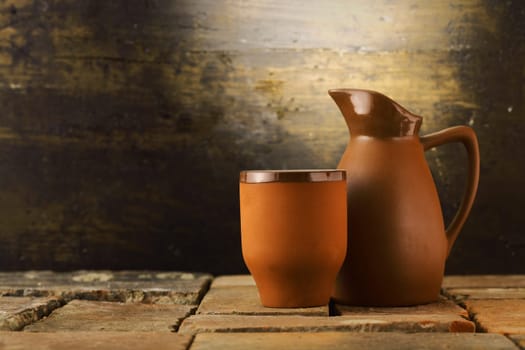 Earthenware mug and pitcher standing on grunge flagstones or tiles in a rustic cellar with copyspace