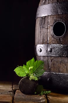Old oak wine barrel with fresh young vine leaves balanced on the bung off a grapevine standing on old bricks against a dark background with copyspace