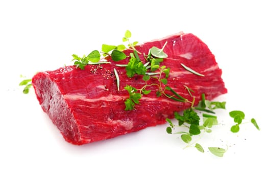 Succulent portion of lean raw fillet steak for a healthy red meat meal garnished with fresh green herbs on a white background