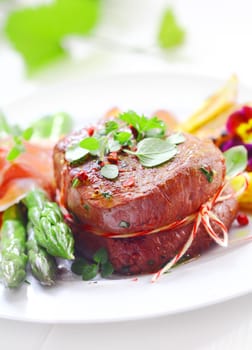 Succulent tender fillet steak medallion tied with string and served with fresh green asparagus spears wrapped in thinly sliced ham or bacon