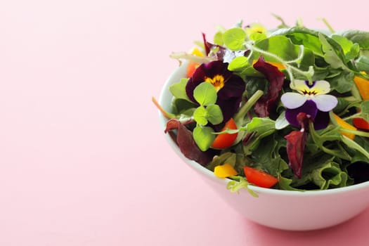 White ceramic bowl filled with a delicious fresh herb and nasturtium salad, high angle view on a studio background with copyspace