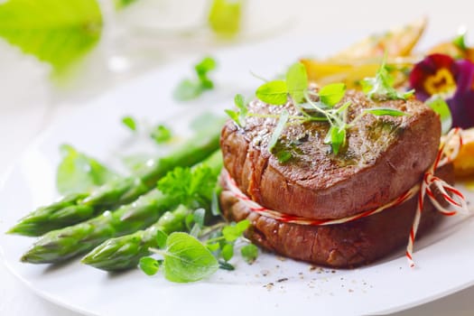 Medallion of roast fillet steak tied with string and served with fresh green asparagus tips and spears liberally garnished with fresh herbs