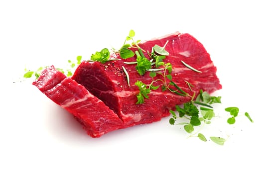 Portion of fresh uncooked fillet steak garnished with herbs with one slice cut through for an individual portion, on a white background