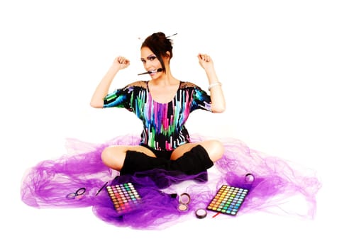 A young woman sitting on lilac twill on the floor with crossed legs and black long boots putting on her makeup, holding up her hands.