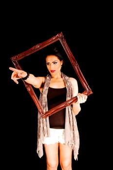 A lovely young woman in white shorts, brown t-shirt and a scarf, holding a brown picture frame for black background, pointing with her finger.