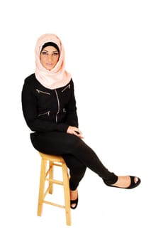A young lovely teenager girl in a black jacket and tights and a pink headscarf  sitting on a chair for a portrait shoot for white background.