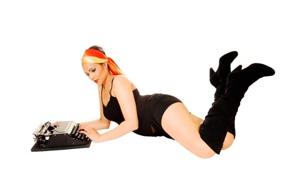 A pretty girl in black shorts and long boots lying on the floor for white background and typing on an old typewriter.