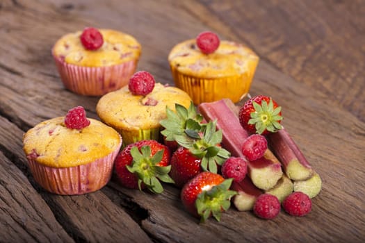 Four strawberry-rhubarb-raspberry muffins with fresh fruit on a wooden background