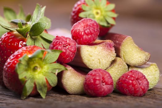 Macro shot of fresh strawberries,rhubarb sticks and raspberries on wooden background