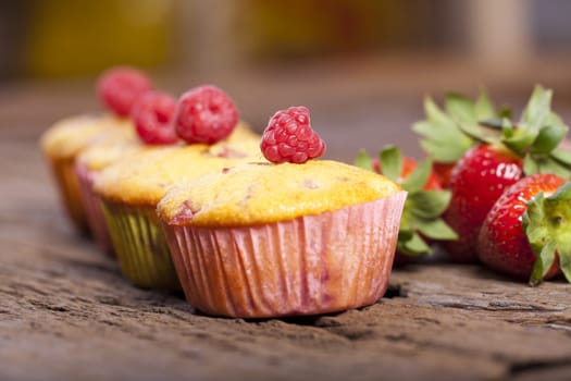 Four strawberry,rhubarb,raspberry muffins in a row with fresh fruits in the background
