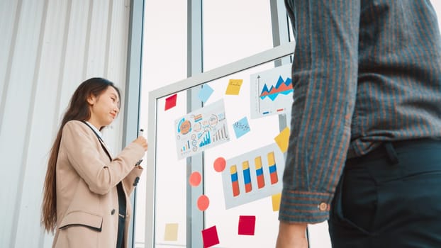 Business people work on project planning board in office and having conversation with coworker friend to analyze project development . They use sticky notes posted on glass to make it organized. Jivy