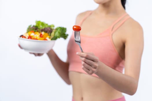 Young sporty Asian woman in sportswear holding salad bowl fill with vibrant of fruit and vegetable. Natural youthful and fit body lifestyle with balance nutrition on isolated background. Vigorous