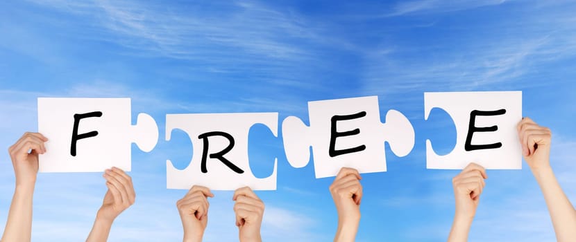 hands holding four pieces of a puzzle with the letters free on it, sky background