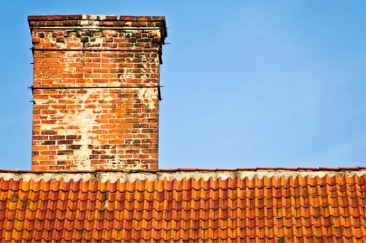 red and orange roof top of old house with brick chimney and blue sky in background