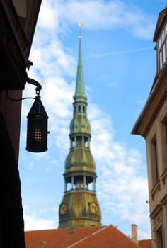 view of sacred Peter church tower with blue cloudy sky in background from old street in Riga, Latvia