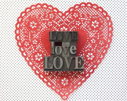 the word 'love' in old metal type on a Valentine doily against a polka dot background