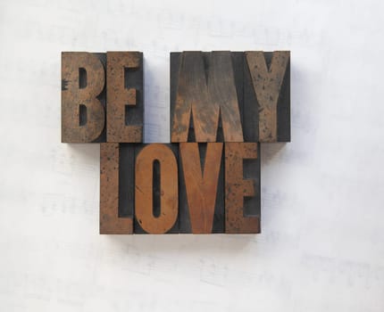the words 'be my love' in old wood type on a faded sheet music background