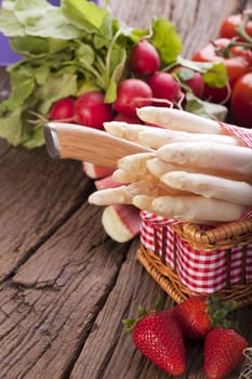 Fresh asparagus with knife in a basket in front of it some strawberries in the background other vegetables and fruits
