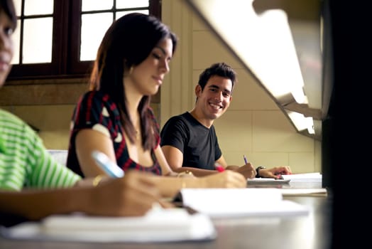 Happy student studying and writing, portrait of hispanic young man doing homework in college library and smiling at camera
