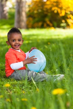 Outdoor portrait of a cute young  little black boy playing with a balloon - African people
