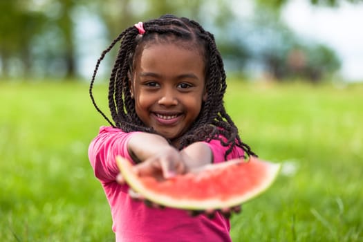 Outdoor portrait of a cute young black little  girl eating watermelon - African people