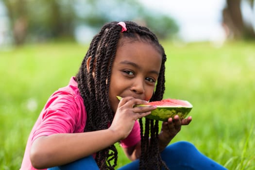 Outdoor portrait of a cute young black little  girl eating watermelon - African people