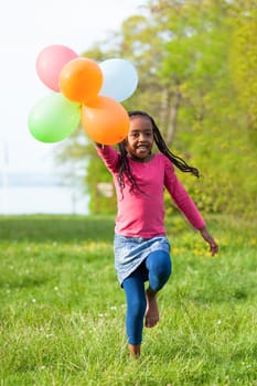 Outdoor portrait of a cute young  little black girl playing with balloons - African people